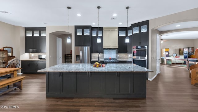 kitchen with dark wood-type flooring, decorative backsplash, a center island with sink, and stainless steel appliances