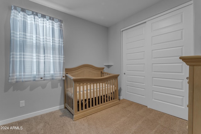 bedroom with light colored carpet, a closet, and a crib