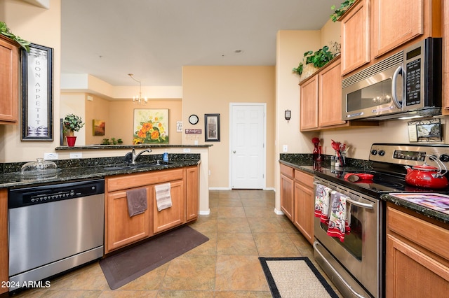 kitchen with sink, decorative light fixtures, dark stone countertops, appliances with stainless steel finishes, and a notable chandelier