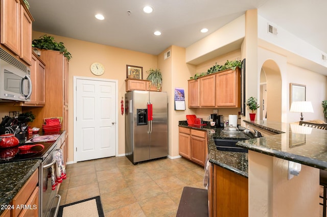 kitchen featuring dark stone counters, a kitchen breakfast bar, sink, kitchen peninsula, and stainless steel appliances