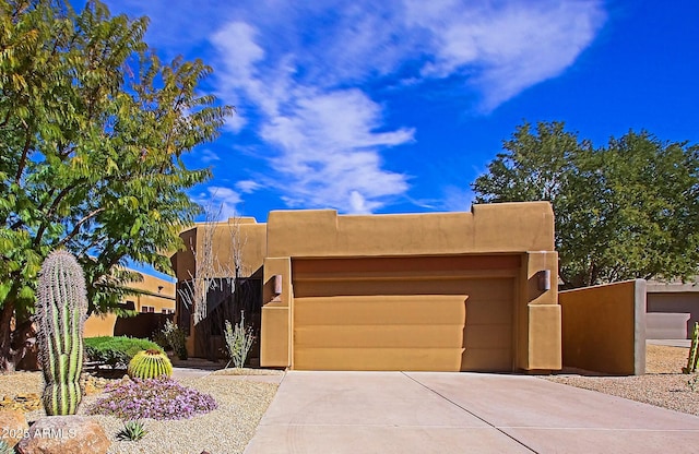 pueblo-style house featuring driveway, an attached garage, and stucco siding