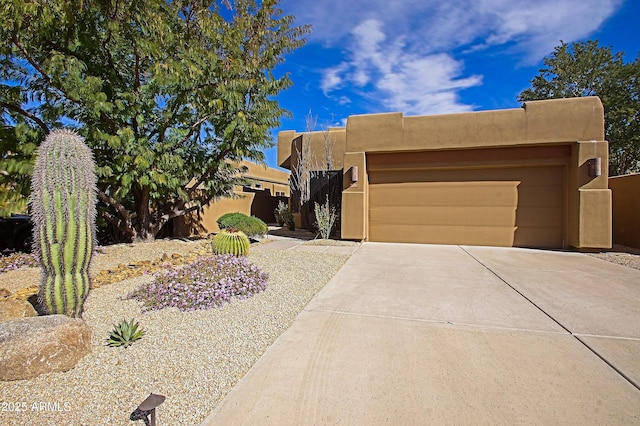 pueblo-style house featuring a garage, driveway, and stucco siding