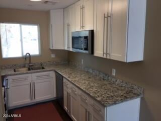 kitchen with light stone countertops, sink, and white cabinets