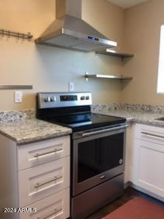 kitchen featuring electric stove, white cabinetry, light stone counters, and wall chimney range hood