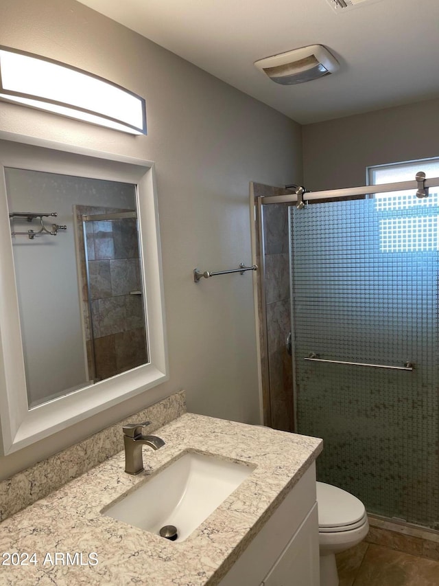 bathroom with tile patterned floors, vanity, a shower with shower door, and toilet