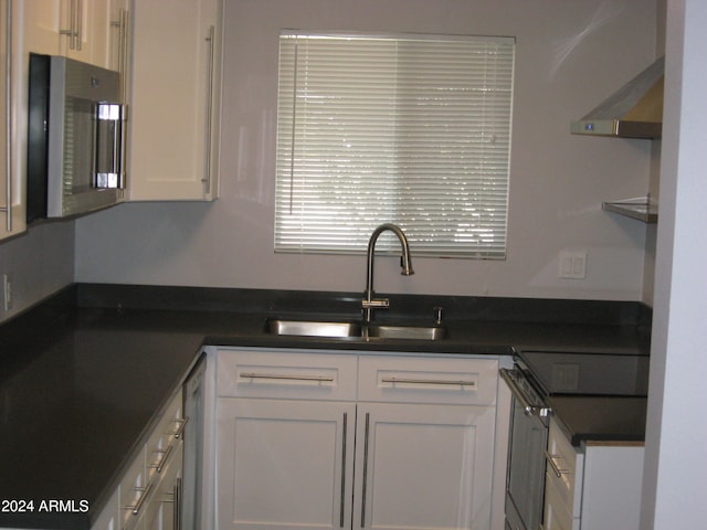 kitchen with appliances with stainless steel finishes, white cabinetry, wall chimney exhaust hood, and sink