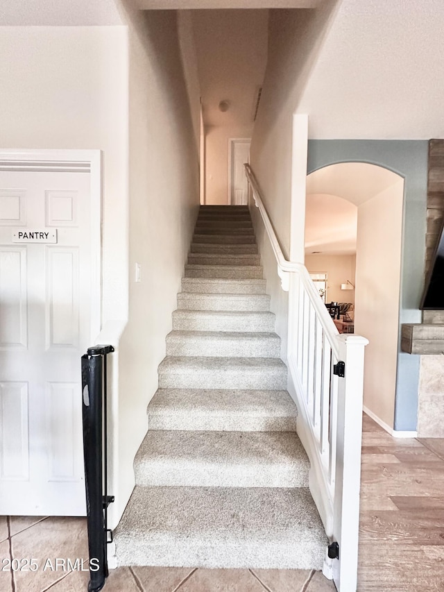 stairway featuring arched walkways and wood finished floors