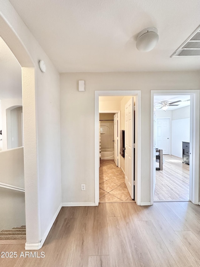 hall with wood finished floors, baseboards, visible vents, and arched walkways