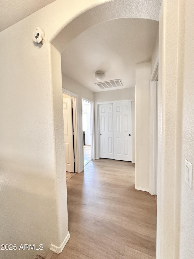 hall with arched walkways, visible vents, wood finished floors, and baseboards