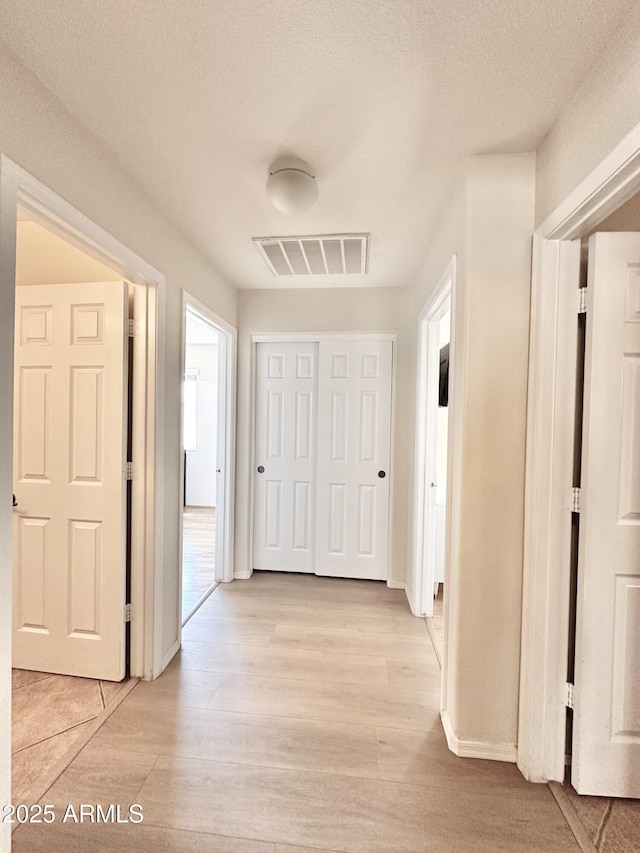 hall with light wood finished floors, visible vents, and baseboards