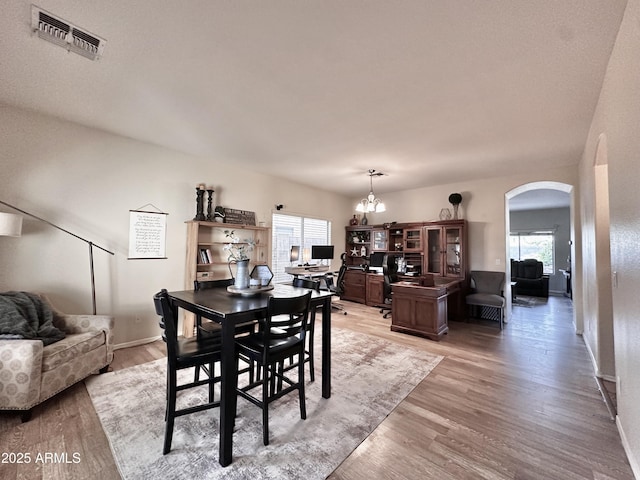 dining room with light wood finished floors, arched walkways, visible vents, and baseboards