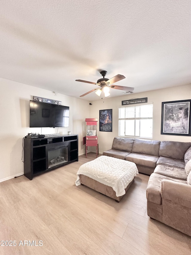 living area featuring a textured ceiling, a ceiling fan, light wood finished floors, and baseboards