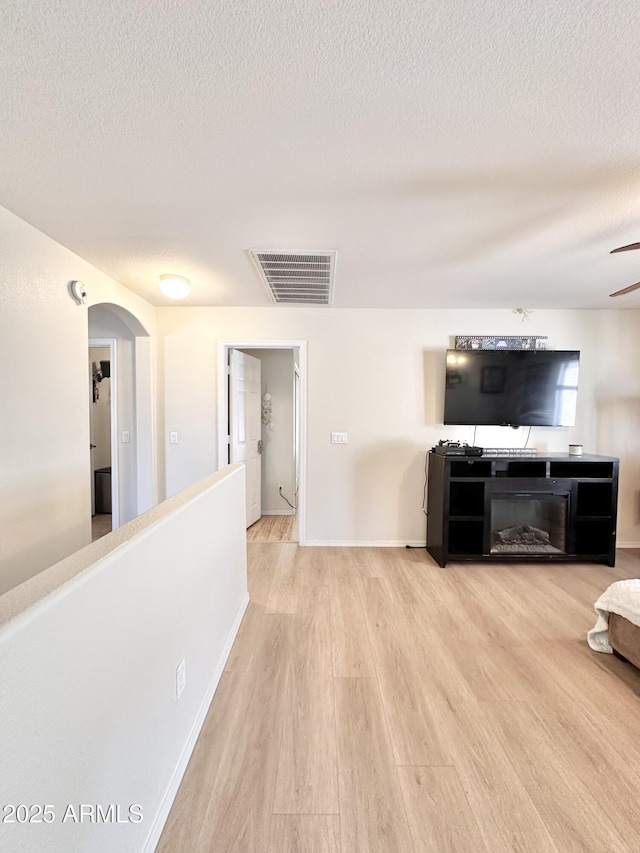 unfurnished living room with a textured ceiling, visible vents, wood finished floors, and arched walkways