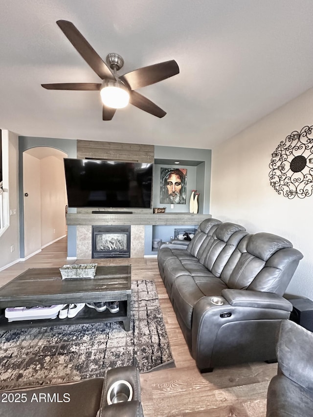 living room with arched walkways, ceiling fan, wood finished floors, and a fireplace