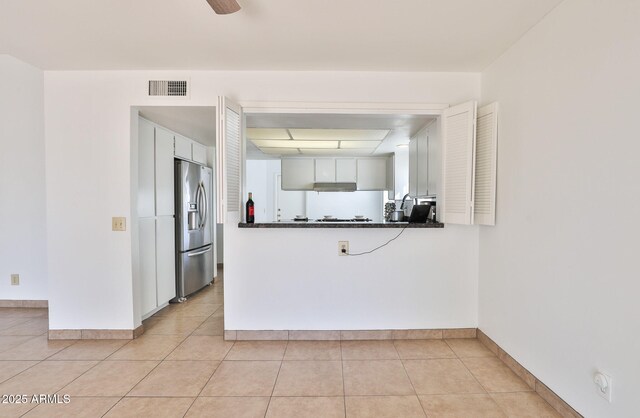 kitchen featuring light tile patterned floors, baseboards, stainless steel fridge with ice dispenser, dark countertops, and white cabinetry