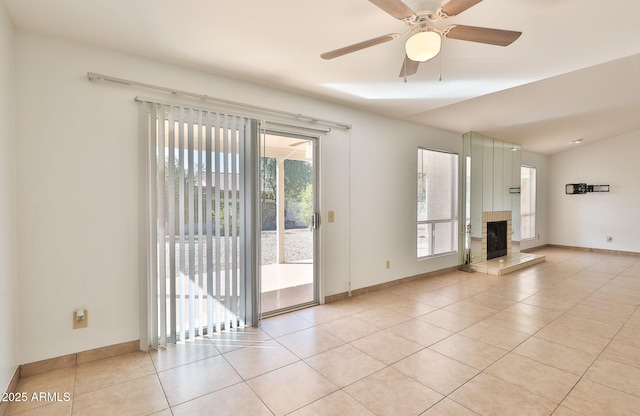 interior space with light tile patterned floors, baseboards, a fireplace with raised hearth, and a ceiling fan