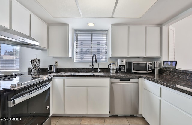 kitchen featuring stainless steel appliances, white cabinets, light tile patterned flooring, a sink, and wall chimney exhaust hood