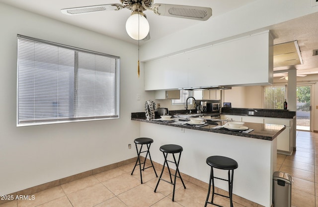 kitchen featuring a breakfast bar area, light tile patterned floors, dark countertops, ceiling fan, and a peninsula