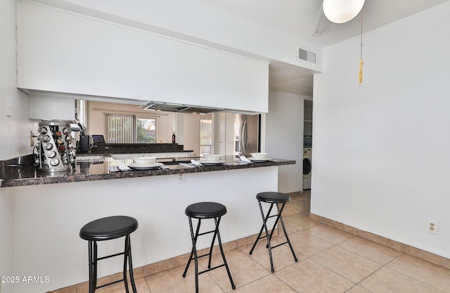 kitchen featuring light tile patterned floors, stainless steel fridge, visible vents, a peninsula, and a kitchen bar