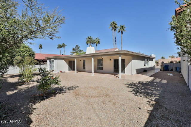 back of house with stucco siding, a chimney, fence, and a patio