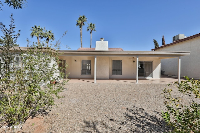 rear view of house featuring central air condition unit, stucco siding, a chimney, and a patio