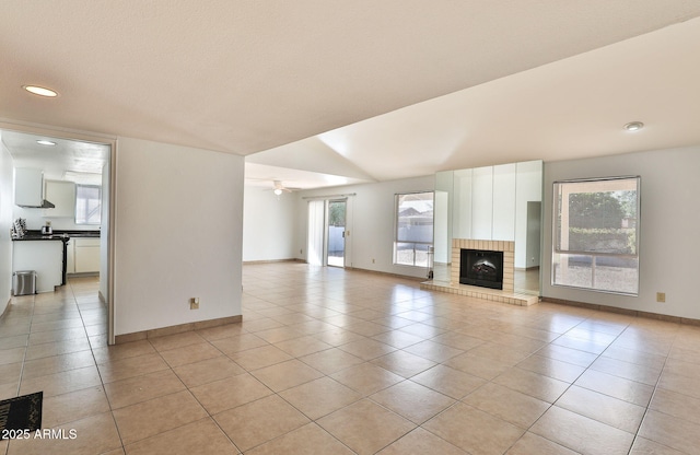 unfurnished living room featuring a ceiling fan, a wealth of natural light, light tile patterned flooring, and a fireplace