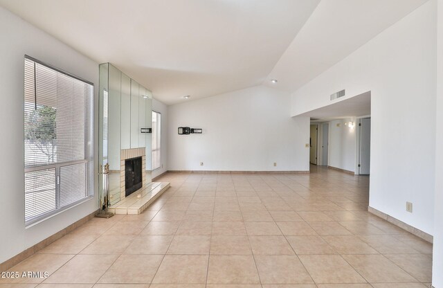 unfurnished living room with light tile patterned floors, baseboards, visible vents, a fireplace with raised hearth, and vaulted ceiling