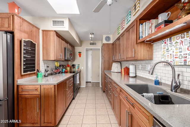 kitchen featuring appliances with stainless steel finishes, a skylight, tasteful backsplash, sink, and light tile patterned floors