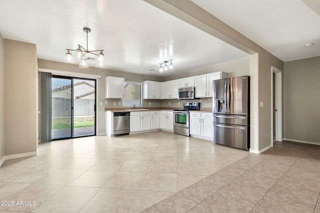 kitchen with sink, appliances with stainless steel finishes, white cabinetry, hanging light fixtures, and light tile patterned flooring