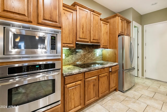 kitchen featuring tasteful backsplash, dark stone counters, appliances with stainless steel finishes, light tile patterned flooring, and brown cabinetry