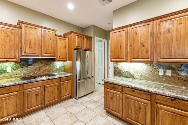 kitchen with brown cabinetry, visible vents, freestanding refrigerator, black electric stovetop, and backsplash