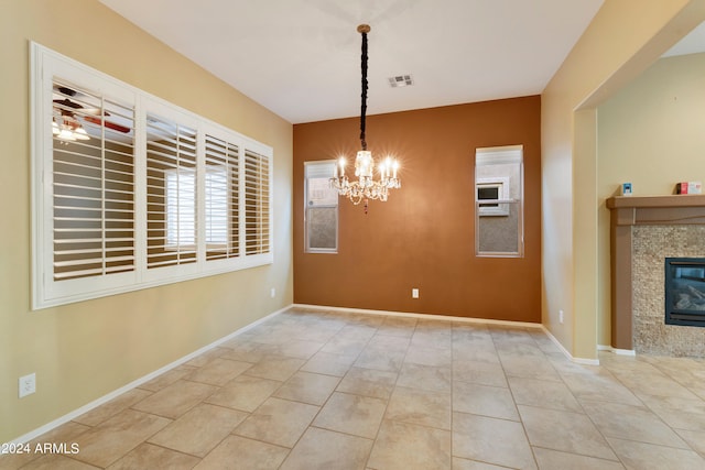 unfurnished dining area with tile patterned flooring, visible vents, baseboards, an inviting chandelier, and a glass covered fireplace