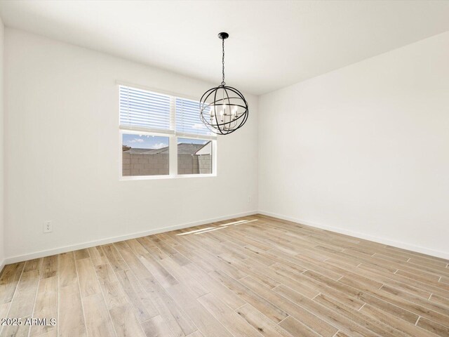 spare room with light wood-style floors, an inviting chandelier, and baseboards