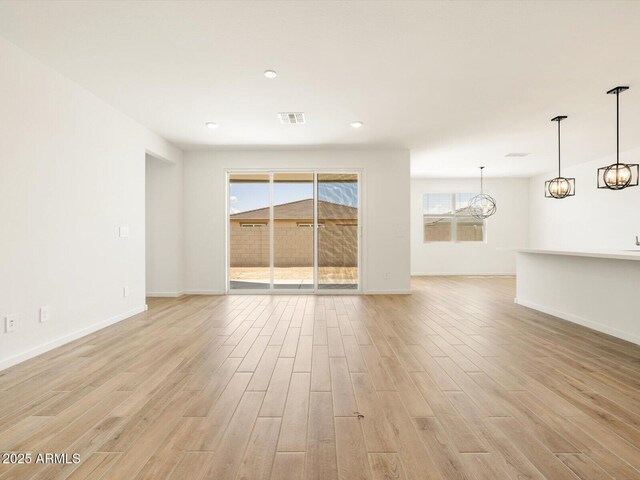 unfurnished living room featuring a chandelier, light wood-type flooring, baseboards, and visible vents