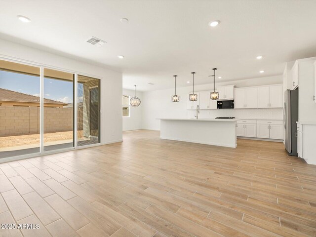kitchen featuring open floor plan, freestanding refrigerator, backsplash, visible vents, and light wood finished floors