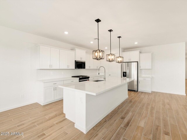 kitchen with gas stove, stainless steel refrigerator with ice dispenser, a center island with sink, light wood finished floors, and a sink