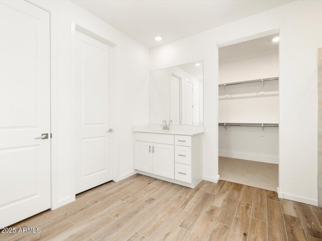 interior space featuring a closet, baseboards, a sink, a spacious closet, and light wood finished floors