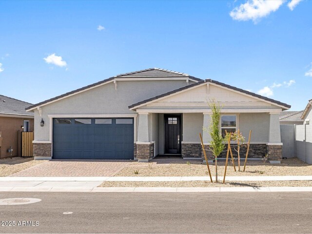 view of front of home with a tiled roof, an attached garage, stone siding, stucco siding, and decorative driveway