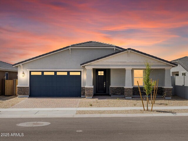 view of front of house featuring stucco siding, stone siding, decorative driveway, a tile roof, and a garage