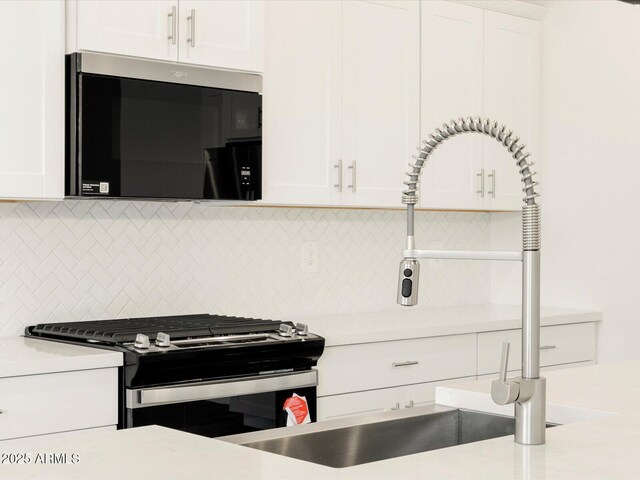 kitchen with stainless steel gas range oven, light countertops, backsplash, white cabinets, and a sink