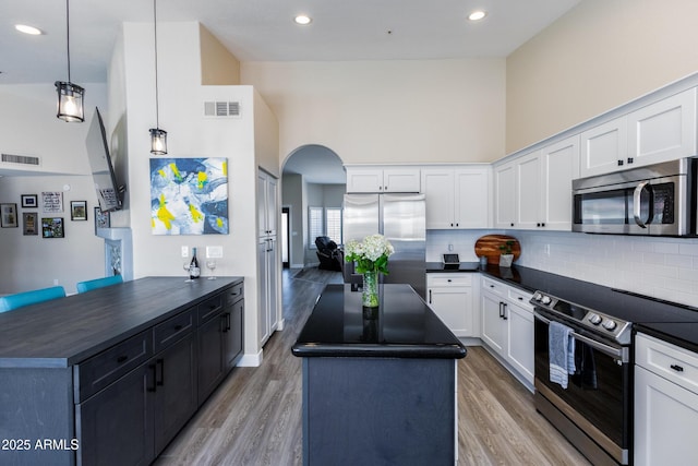 kitchen featuring dark countertops, visible vents, a center island, arched walkways, and stainless steel appliances