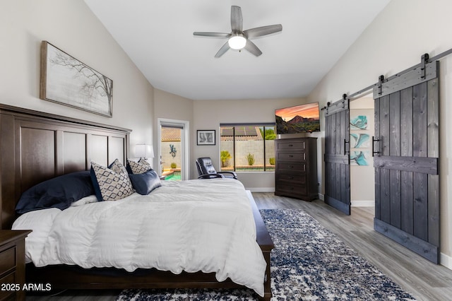 bedroom featuring a ceiling fan, baseboards, lofted ceiling, light wood-style flooring, and a barn door