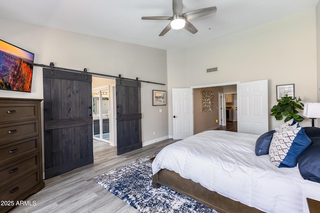 bedroom with visible vents, baseboards, lofted ceiling, a barn door, and light wood-style flooring