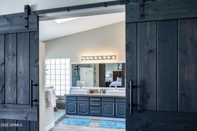 full bath with a sink, lofted ceiling, wood finished floors, and double vanity