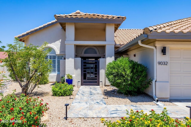 doorway to property with stucco siding, a tiled roof, and a garage