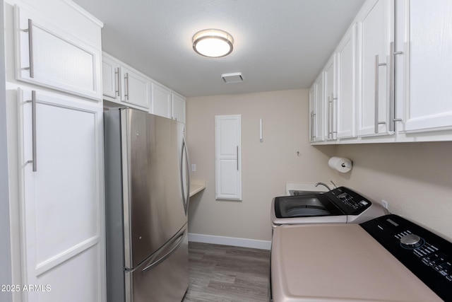 clothes washing area with wood finished floors, baseboards, visible vents, cabinet space, and separate washer and dryer