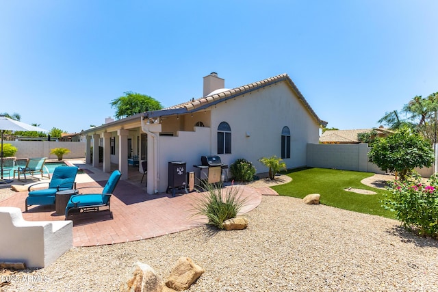 back of property with a tile roof, stucco siding, a chimney, a fenced backyard, and a patio