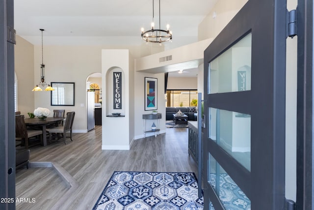 foyer featuring visible vents, arched walkways, light wood finished floors, baseboards, and a chandelier