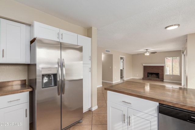 kitchen with light tile patterned floors, wooden counters, ceiling fan, a brick fireplace, and stainless steel fridge