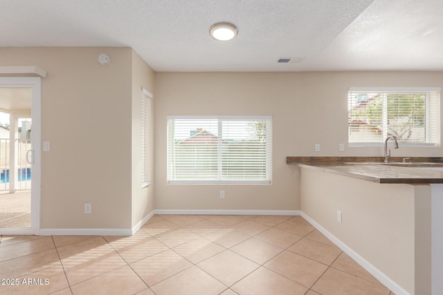 kitchen with a sink, plenty of natural light, a textured ceiling, and light tile patterned flooring